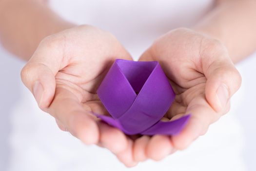 World cancer day, hands holding purple ribbon on grey background. Healthcare and medical concept.