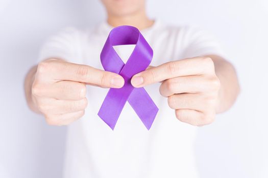 World cancer day, hands holding purple ribbon on grey background with copy space for text. Healthcare and medical concept.