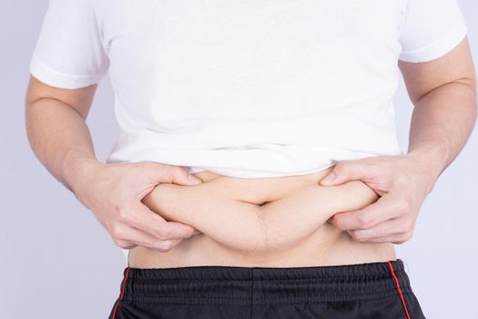 Fat man holding excessive fat belly, overweight fatty belly isolated grey background. Diet lifestyle, weight loss, stomach muscle, healthy concept.