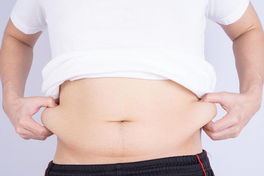 Fat man holding excessive fat belly, overweight fatty belly isolated grey background. Diet lifestyle, weight loss, stomach muscle, healthy concept.