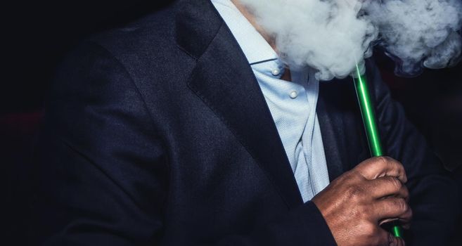 a man with no face smokes a hookah slowly exhaling smoke at the nightclub