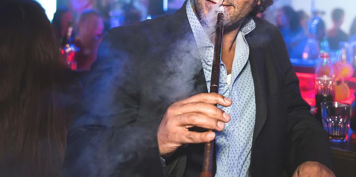 a man with no face smokes a hookah slowly exhaling smoke at the nightclub