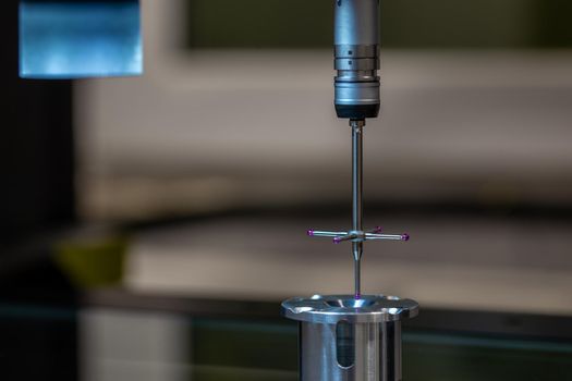 CMM - Coordinate Measuring Machine - contact probe measure aluminium sample part on glass table surface. High precision production metrological control process. Close-up macro shot with background blur.
