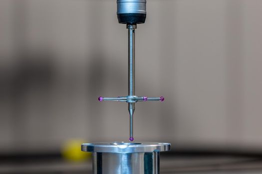 CMM - Coordinate Measuring Machine - contact probe measure aluminium sample part on glass table surface. High precision production metrological control process. Close-up with background blur.