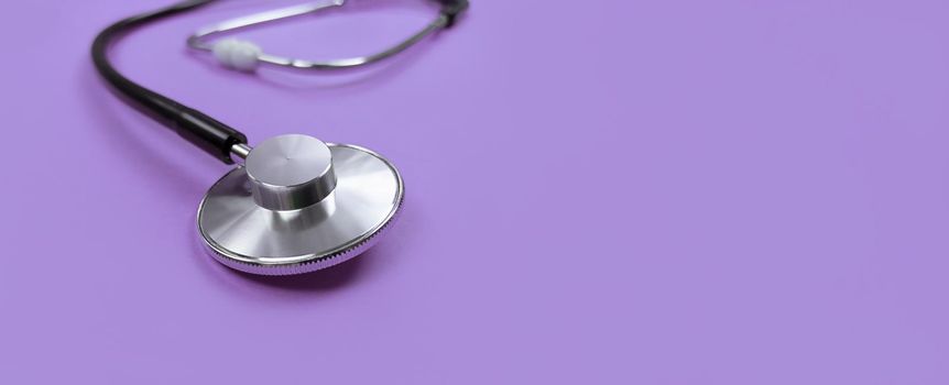 Black stethoscope on a purple background with copy space.
