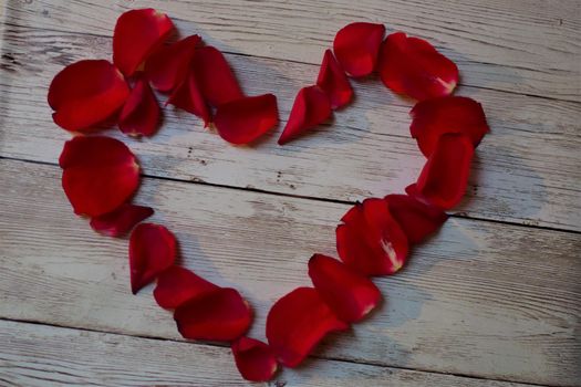 View from above on red rose petals heart on a textured beige background with copy space