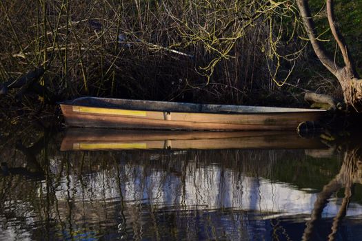 Old row boat on the bank of a river refleceted in the water