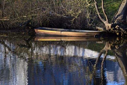 Old row boat on the bank of a river refleceted in the water
