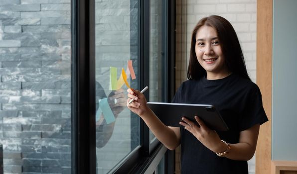 Portrait business woman using tablet during post it notes idea discussing and planning in glass wall at meeting room, business concept