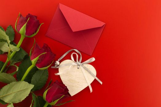 Red roses, envelope and wooden heart medallion on red background with free copy space. Wishes, greetings and love message