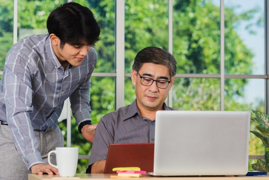 Asian senior and junior two businessmen discuss something during their meeting consultation project, Mature boss with a business partner working together on the laptop computer on desk home office