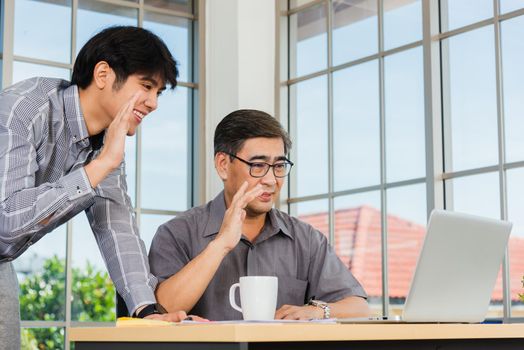 Asian senior and young business man working online on a modern laptop computer he looking the screen meeting online. Old and junior businessman using video call conference on desk table at office