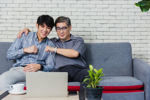 Asian senior businessman with laptop computer discuss together with young team in office. Father man and his son sit on sofa talking chatting on video call conference on laptop in living room at home