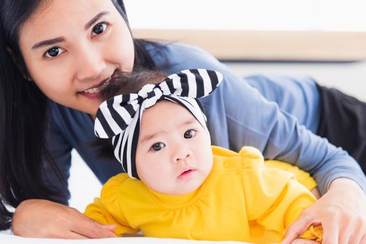 Portrait of beautiful young Asian mother playing and smiling together with his newborn little baby at home, Parent mom and little kid relaxing in the bedroom, Family having fun together