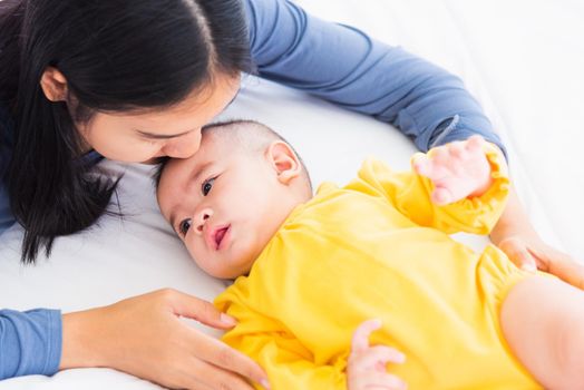 Portrait of beautiful young Asian mother kissing her infant newborn baby in a white bed, The mom loves his child, Healthcare and medical and mother day concept