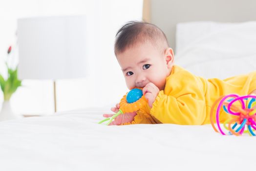 Portrait of beautiful young Asian newborn little baby prone on the bed at home, Happy baby smile wears a yellow shirt relaxing in the room, Family morning at home