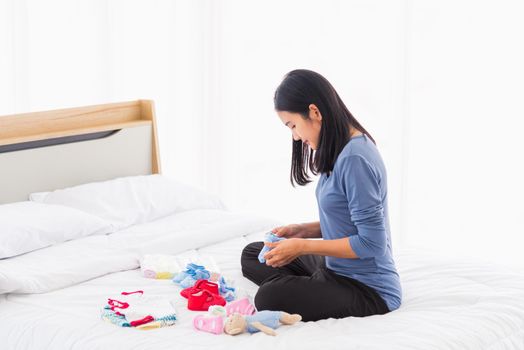 Asian mother preparing baby clothes resting and relaxing on the bed she makes purchase new baby clothes for after baby getting ready for newborn birth