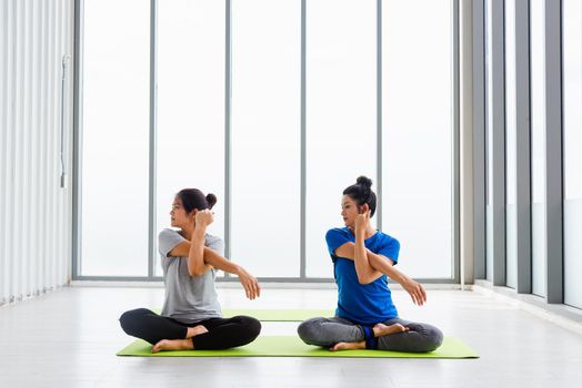 Two Asian women sporty attractive people practicing yoga lesson together, working out at the fitness GYM, Young and senior female exercising do yoga in yoga classes, sport healthy lifestyle