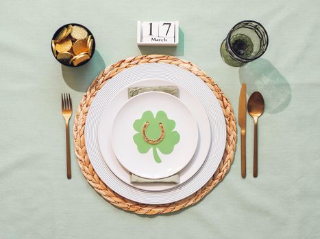 Beautiful festive table setting for St.Patrick's day with cutlery and lucky symbols. Top view of Saint Patrick's day holiday table with green linen tablecloth. Flat lay.