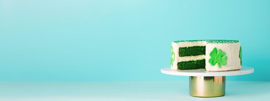 St Patricks Day sweet food concept. Green velvet cake decorated green shamrock leaves for Saint Patrick's Day party on blue background. Copy space. Long horizontal banner