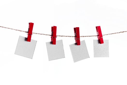 Set of four white blank paper notes held on a string with red clothespins isolated on white background