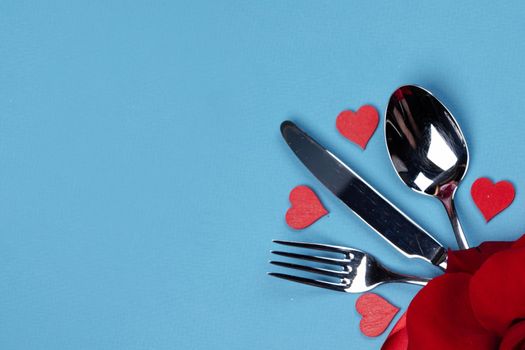 Cutlery set tied with silk ribbon rose flower and hearts on blue background Valentine day romantic dinner concept