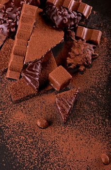 Broken chocolate pieces and cocoa powder on wooden background