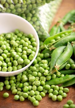 RAW baby peas in small white bowl, over retro wooden boards. Close-up