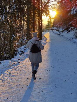 Woman hiking on snow in white winter forest berore the sunset. Recreation and healthy lifestyle outdoors in nature.