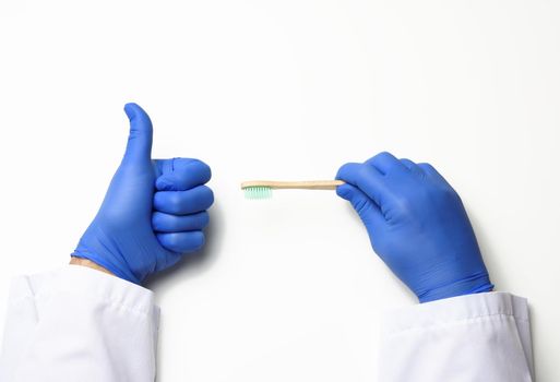 doctor therapist is dressed in a white robe uniform and blue sterile gloves holding a toothbrush, daily brushing concept, white background