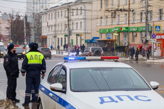 TULA, RUSSIA - JANUARY 23, 2021: Russian road police officers standing near patrol car and dirty snow on winter city road - close-up with selective focus on roof lamp. Letters DPS mean Traffic Patrol Police