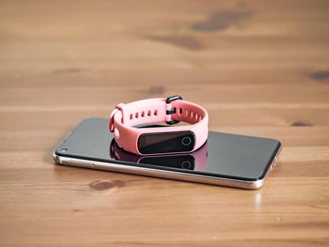 Fitness tracker on smartphone wooden tabletop. Pink female pedometer or wearable device on smartphone with infinity display, copy space