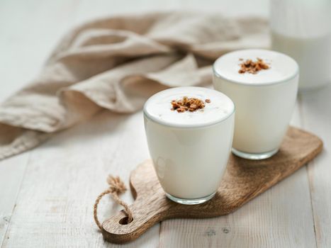 Kefir, buttermilk or yogurt with granola. Yogurt in glass on white wooden background. Probiotic cold fermented dairy drink. Gut health, fermented products, healthy gut flora concept. Copy space