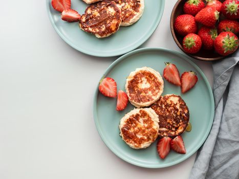 Sweet cheese pancakes on plate served strawberries. Cottage cheese pancakes, syrniki, ricotta fritters, curd fritters. Top view or flat lay. Copy space for text or design.