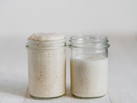 Two glass jars with wheat sourdough starters in different hydration levels. Starter 100 percent hydration (left) and starter with higher hydration (right). Copy space