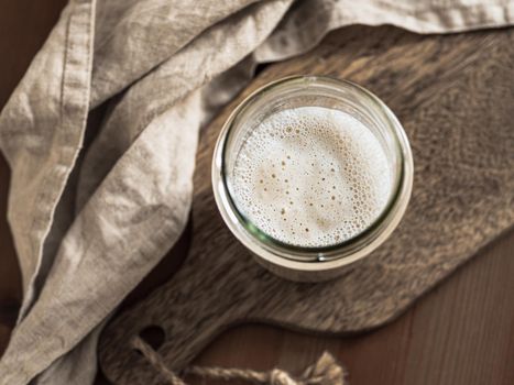Wheat sourdough starter. Top view of glass jar with sourdough starter on wooden cutting board. Copy space for text or design.