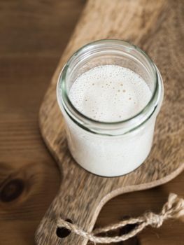 Wheat sourdough starter. Glass jar with sourdough starter on wooden cutting board over wooden tabletop. Copy space for text or design. Vertical.