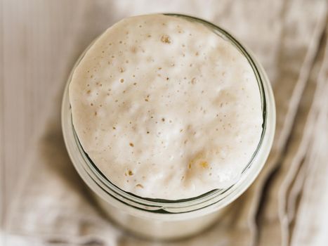 Wheat sourdough starter. Top view of glass jar with sourdough starter on white wooden background. Copy space for text or design.