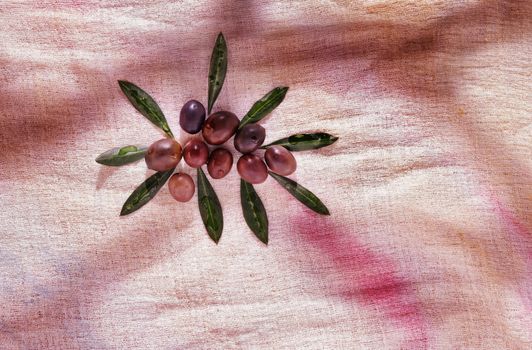 Group of black olives on colored cotton cloth , green leaves surround the olives 