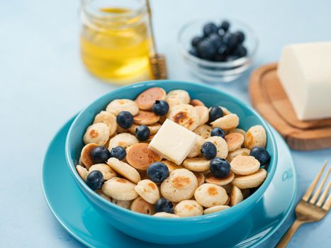Trendy food - pancake cereal. Heap of mini cereal pancakes in boul on blue background. Copy space for text or design