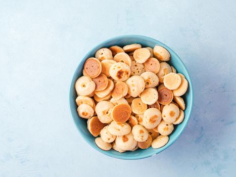 Trendy food - pancakes cereal. Heap of mini cereal pancakes in boul on blue background. Copy space left for text. Top view or flat lay.