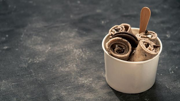 Rolled ice cream with in cone cup on dark rustic background. Iced rolls with biscuits chocolate sandwich cookies. Thai style rolled ice cream with copy space for text or design. Banner.