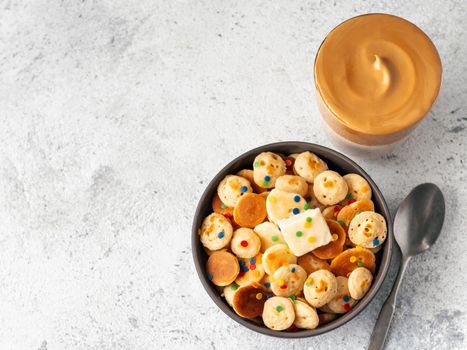 Mini pancakes cereal and dalgona coffee on gray cement background copy space. Trendy food and drink - tiny panckakes and whipped instant coffee with milk or korean dalgona coffee. Top view or flat lay
