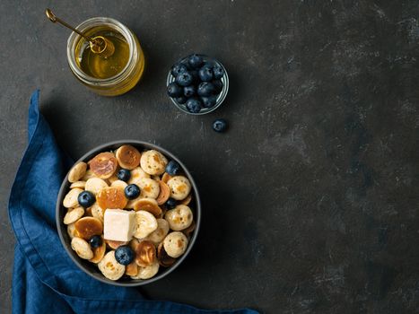 Trendy food - pancakes cereal served butter and blueberries. Heap of mini cereal pancakes in boul on dark background. Copy space right for text. Top view or flat lay.