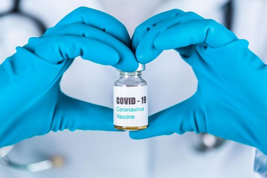 Woman doctor or nurse in uniform and gloves wearing face mask protective in lab holding in a form of heart medicine vial vaccine bottle with COVID-19 Coronovirus vaccine label