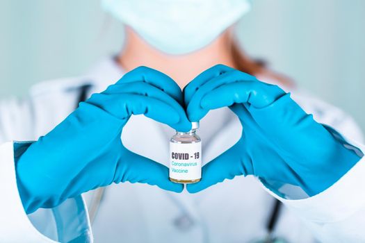 Woman doctor or nurse in uniform and gloves wearing face mask protective in lab holding in a form of heart medicine vial vaccine bottle with COVID-19 Coronovirus vaccine label