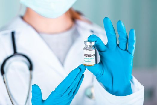 Woman doctor or nurse in uniform and gloves wearing face mask protective in lab holding medicine vial vaccine bottle with COVID-19 Coronovirus vaccine label
