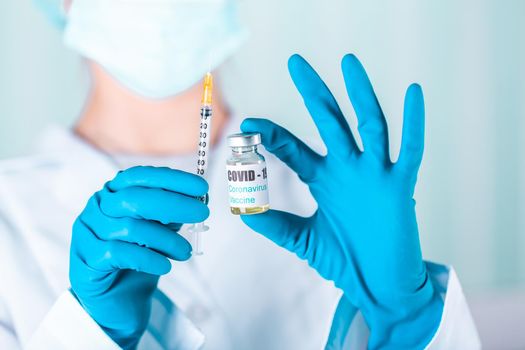 Woman doctor or nurse in uniform and gloves wearing face mask protective in lab holding medicine vial vaccine bottle with COVID-19 Coronovirus vaccine label