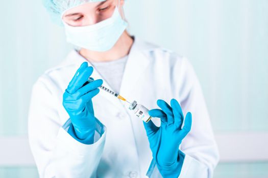 Woman doctor or nurse in uniform and gloves wearing face mask protective in lab holding medicine vial vaccine bottle with COVID-19 Coronovirus vaccine label