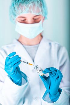 Woman doctor or nurse in uniform and gloves wearing face mask protective in lab holding medicine vial vaccine bottle with COVID-19 Coronovirus vaccine label